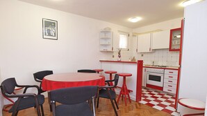 Cocina compacta con una paleta de colores rojo y blanco, un pequeño comedor con una mesa redonda y sillas, y un suelo de madera con patrón de espiga.