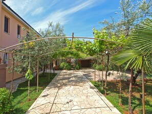 A stone pathway leading to a covered area with a pergola, surrounded by greenery and a building. - Apartment 875 (Fazana)