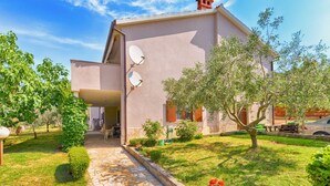 A house with a stone pathway leading to the entrance, surrounded by well-maintained grass and trees. - Apartment 877 (Pula)