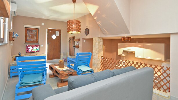 A living room with blue chairs, a wooden table, a grey sofa, and a kitchen area with cabinets. - Apartment 877 (Pula)