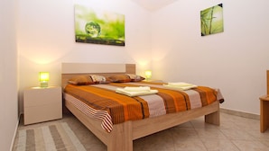 A bedroom with a wooden bed, two bedside tables with lamps, a large window, and two wall-mounted paintings.