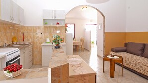 A compact kitchen with a built-in oven, a sink, and a countertop with a fruit bowl. There is a dining area with a table and chairs, and a sofa in the living room.