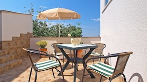 An outdoor patio with a table and chairs, a beige umbrella, and potted plants.