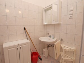 A bathroom with a white sink, mirror, and cabinets. There is a mop and a red bucket on the floor. - Apartment 894 (Medulin)