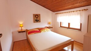 A bedroom with a wooden bed, two bedside lamps, a window with curtains, and a wall-mounted picture of a flower. - Apartment 895 (Medulin)