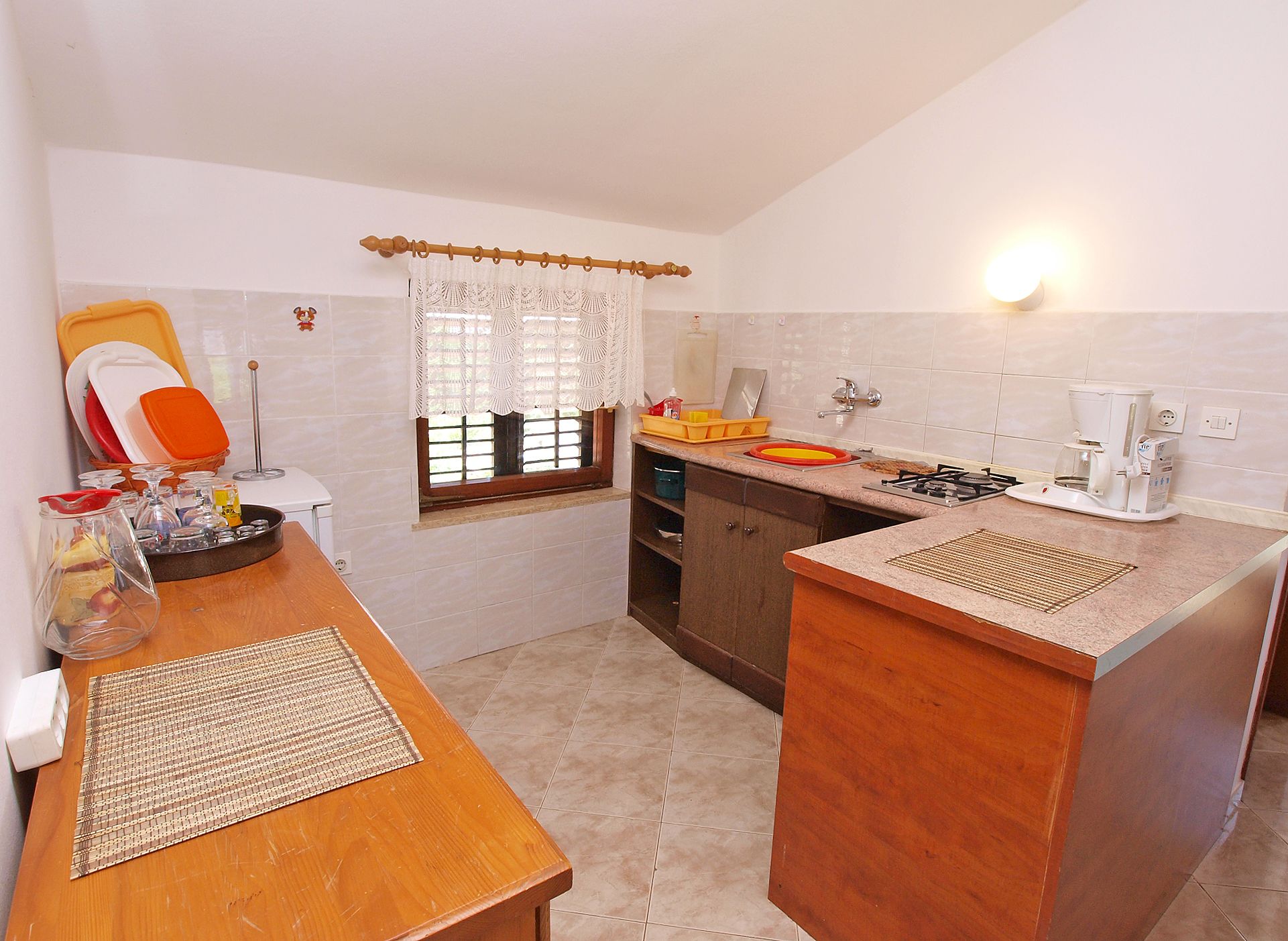 A compact kitchen with a wooden countertop, a coffee maker, and a window with lace curtains.