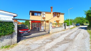 Une maison à deux étages avec une voiture rouge garée devant, une allée en gravier et un ciel bleu dégagé.
