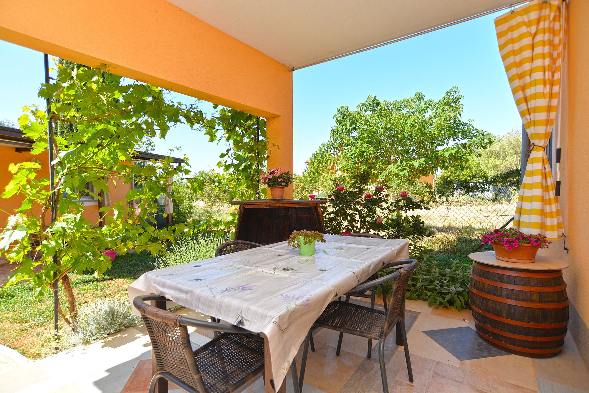 An outdoor patio with a table and chairs, surrounded by greenery and a view of the countryside.