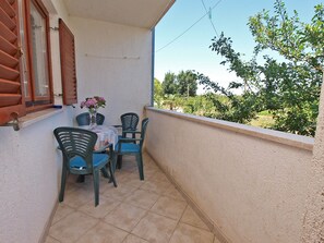 A balcony with a table and chairs, a window with shutters, and a view of greenery. - Apartment 909 (Fazana)