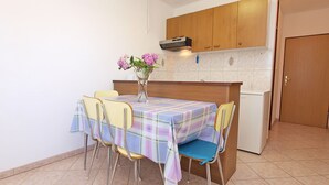 Een kleine keuken met een betegelde vloer, een tafel met geruit tafelkleed, vier stoelen en een koelkast.