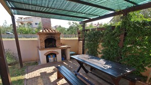 Une terrasse extérieure dotée d’un four en briques, d’une table de pique-nique et d’un espace salon abrité.