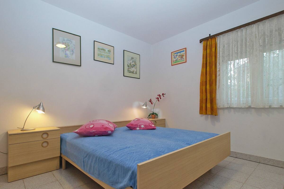 A bedroom with a wooden bed, two bedside tables with lamps, a blue bedspread, and three framed pictures on the wall.