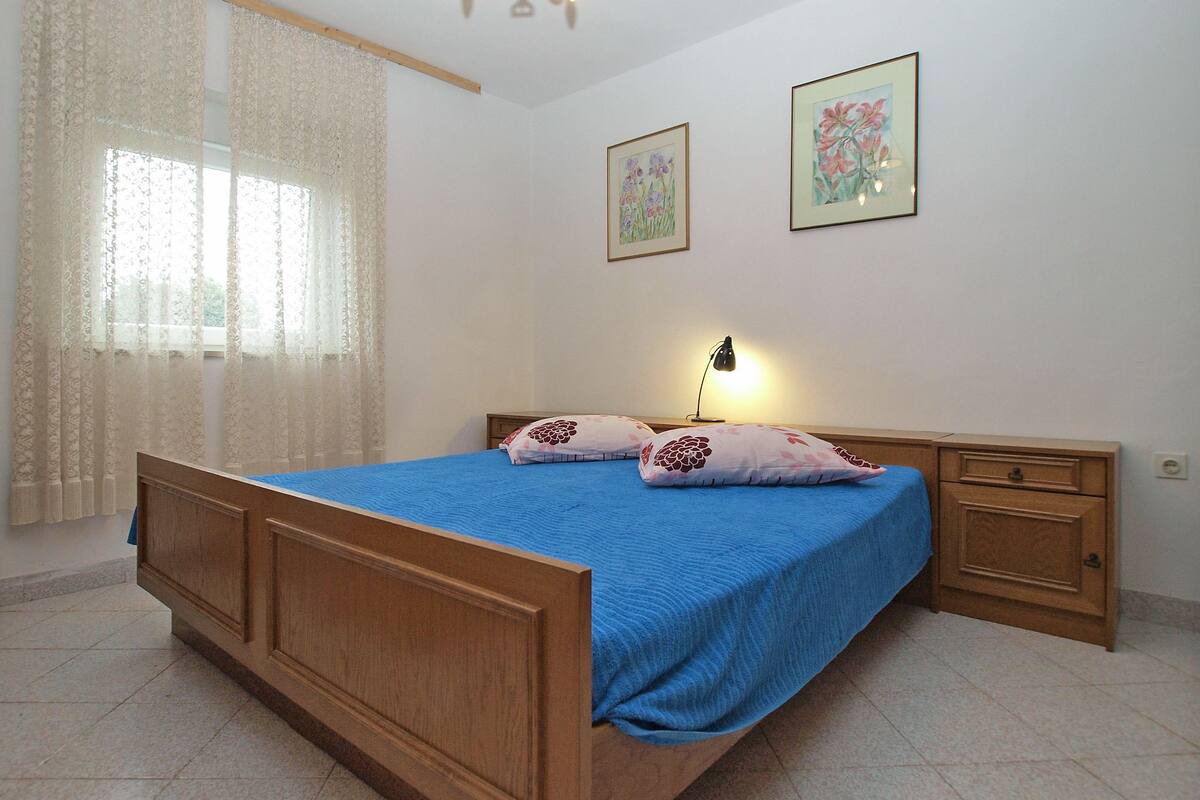 A bedroom with a wooden bed, a bedside table, a lamp, and two framed floral paintings on the wall.