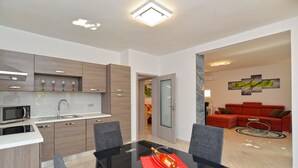 A modern kitchen with a microwave, sink, and wooden cabinets. There is a dining table with chairs and a red placemat. A red sofa and a coffee table are visible in the living area. - Apartment 925 (Fazana)