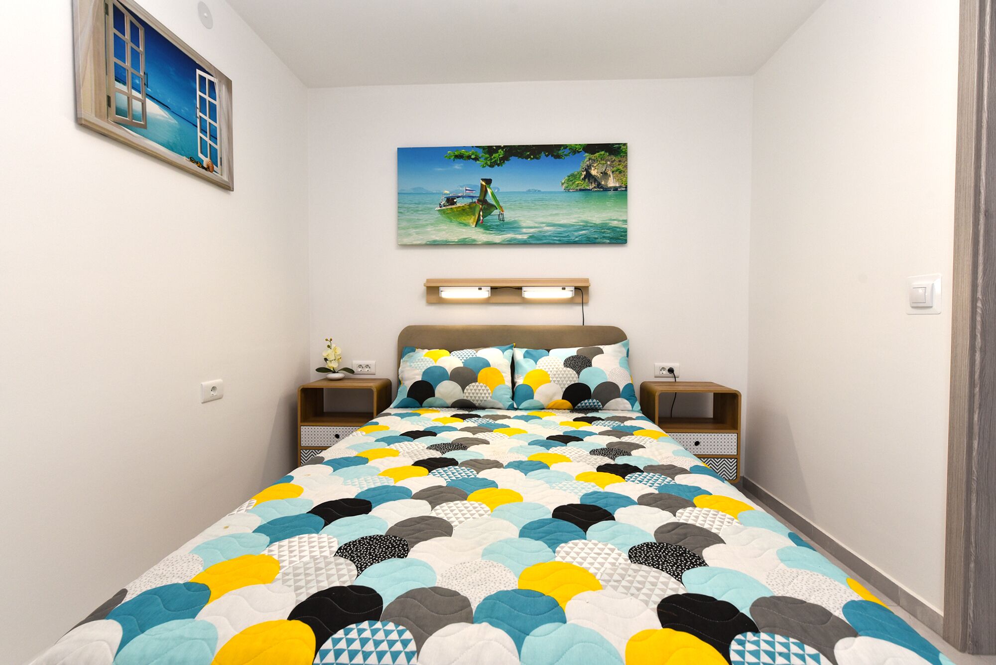 Ein Schlafzimmer mit einem Bett, zwei Nachttischen, einem Wandregal und einem Bild von einer Strandansicht.