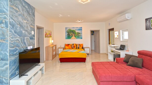 A modern bedroom with a bed, a red sofa, a TV, and a painting of a tropical scene. - Apartment 925 (Fazana)