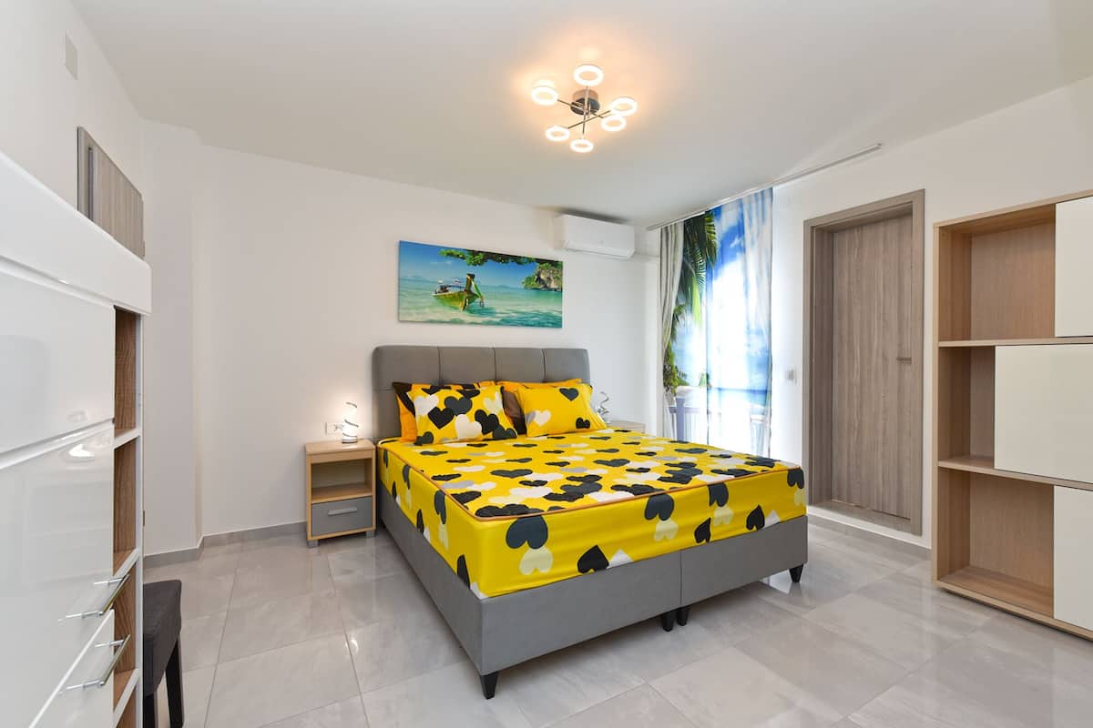 A modern bedroom with a bed, nightstand, and a painting of a tropical scene.