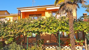 A yellow building with a balcony, surrounded by greenery and a palm tree. - Apartment 933 (Fazana)