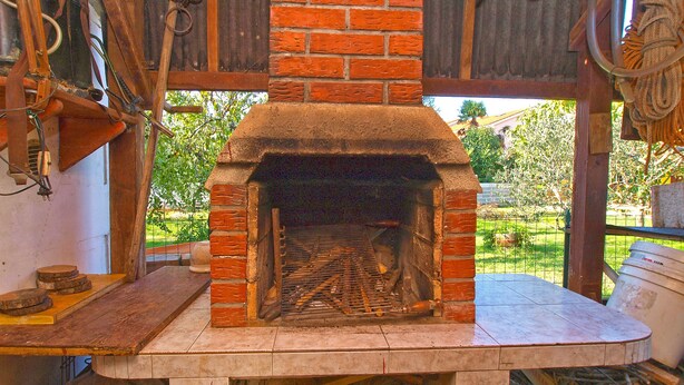 A brick-built wood-fired oven with a stone base, surrounded by tools and materials, indicating a functional space for cooking or baking. - Apartment 933 (Fazana)