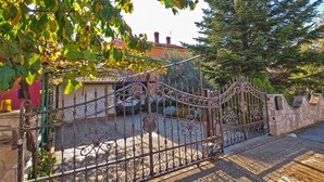 A wrought iron gate with a stone wall, a parked car, and a building with a red facade. - Apartment 933 (Fazana)