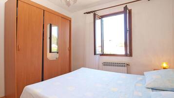 Un dormitorio con cama, armario, ventana y radiador.