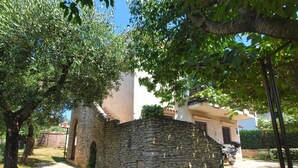 A stone wall with a narrow passageway, surrounded by trees and a building with a white facade. - Apartment 940 (Medulin)