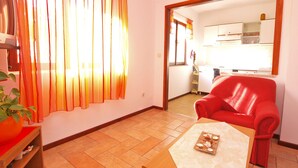 A living room with a red chair, a wooden coffee table with a decorative item, and a window with orange curtains. - Apartment 940 (Medulin)