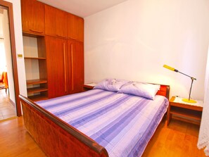 Quarto com estrutura de cama de madeira, colcha listrada, mesa de cabeceira com abajur e guarda-roupa de madeira.