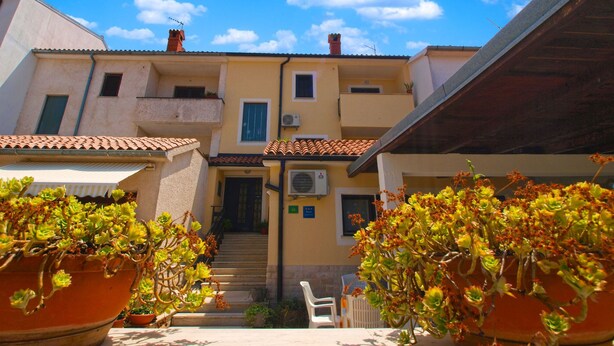 A courtyard with a staircase leading to a building entrance, surrounded by potted plants and a clear blue sky. - Apartment 946 (Pula)