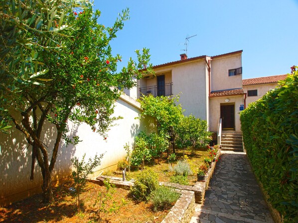 A narrow stone pathway leading to a building with a tiled roof and a balcony.