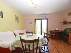 A dining area with a round table, chairs, and a small kitchen area with a computer and a ship model on the wall.