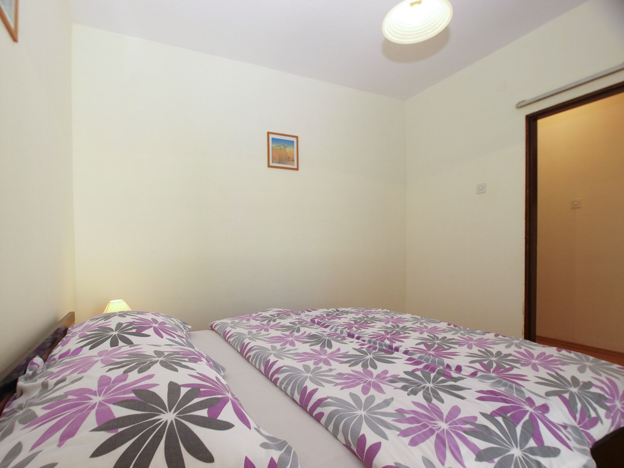 A small, simple room with two beds, a single wall-mounted light, and a door.