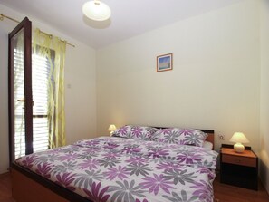 A bedroom with a bed, two bedside tables with lamps, a window with curtains, and a small picture on the wall.