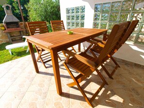 Une table de patio en bois, des chaises, un barbecue et un sol carrelé.