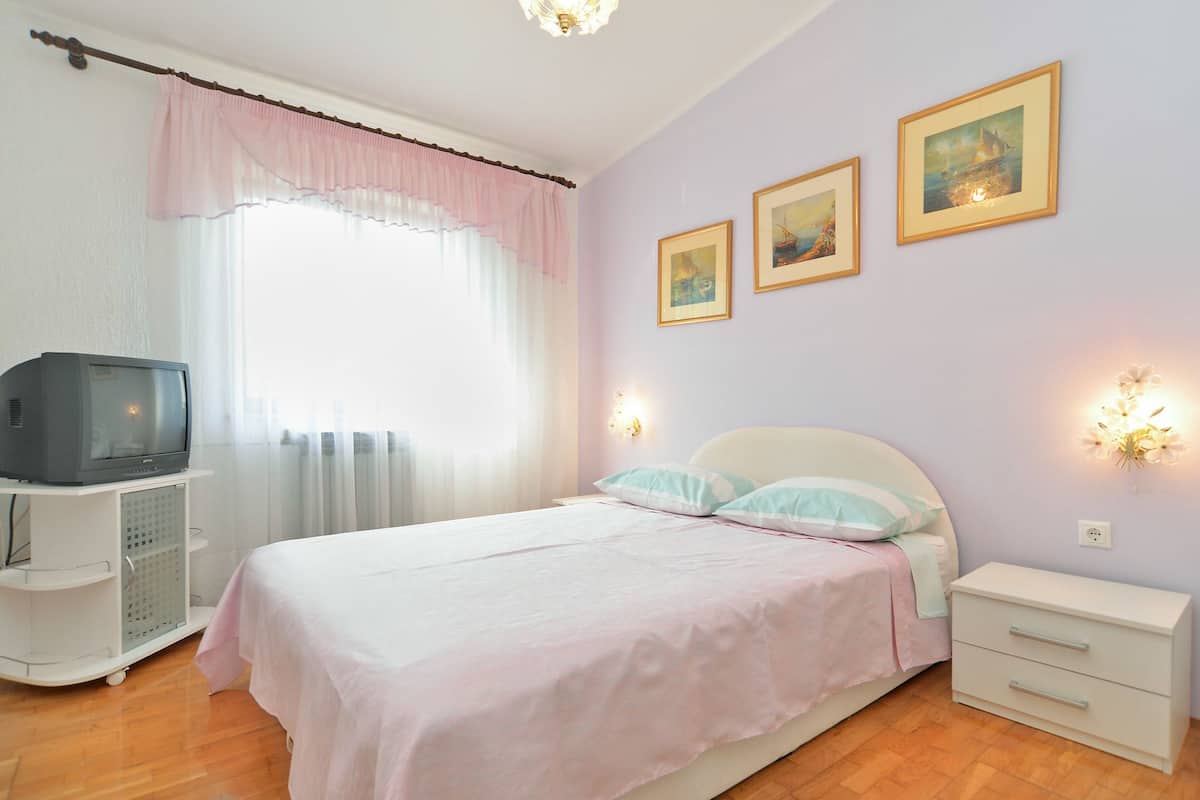 A bedroom with a bed, a TV on a stand, a nightstand, and wall-mounted lights.