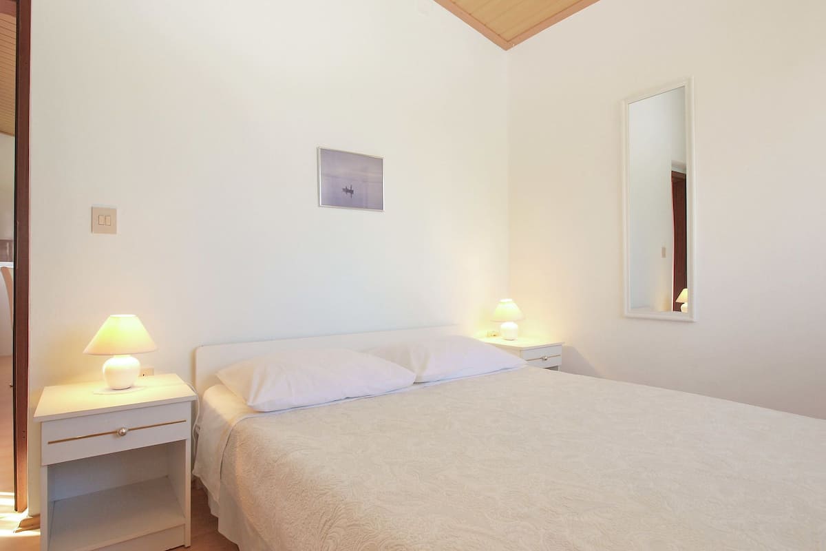 A bedroom with a bed, two bedside tables with lamps, a small wall clock, and a mirror.