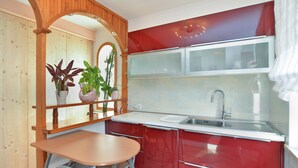 A kitchen with a wooden arch, red cabinets, a stainless steel sink, and a small table with chairs. - Apartment 959 (Vodnjan)