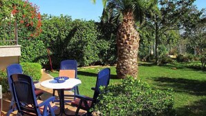An outdoor patio with a round table and four chairs, surrounded by lush greenery and a palm tree. - Apartment 979 (Medulin)