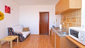 A compact kitchen with wooden cabinets, a microwave, and a sink. There's a small bench and a door leading to another room. - Apartment 990 (Fazana)