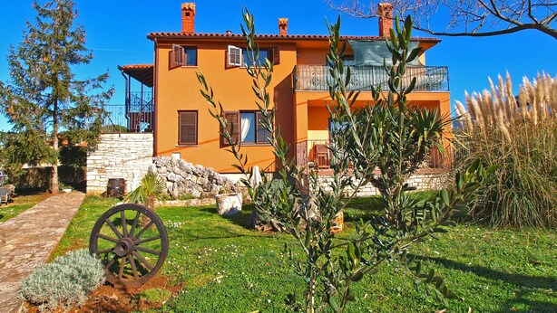 A two-story house with a stone wall and a large wheel in the foreground. - Apartment 990 (Fazana)