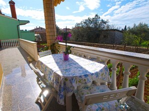 Un balcon avec une table et des chaises, un pot de fleurs et une vue sur les environs, notamment les bâtiments et les arbres.