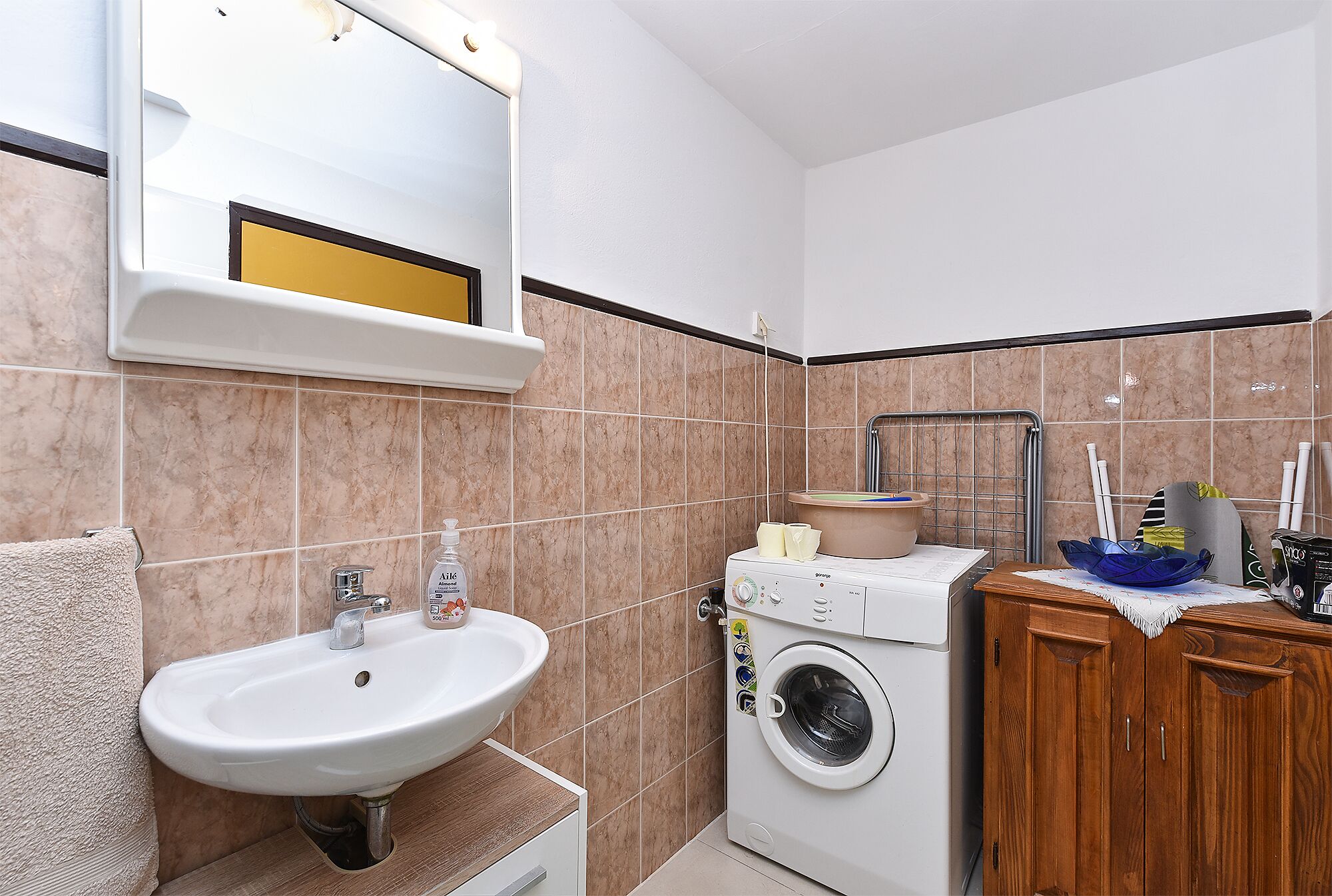 A bathroom with a sink, mirror, washing machine, and wooden cabinet.