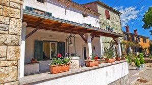 A traditional building with a stone facade, a covered porch with potted plants, and a clear blue sky. - House 1009 (Svetvincenat)