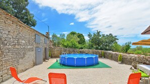 A stone building with a blue above-ground pool, surrounded by gravel and orange chairs. - House 1009 (Svetvincenat)