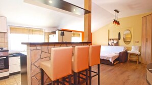 A compact hotel room with a kitchenette, a dining area with bar stools, a bed, and a bathroom with a mirror. - Apartment 1017 (Fazana)