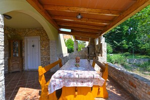 An outdoor dining area with a stone wall, wooden table, and chairs. - Apartment 1017 (Fazana)