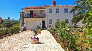 A two-story building with a tiled roof, a balcony with railings, and a paved pathway leading to the entrance. - Apartment 1030 (Fazana)