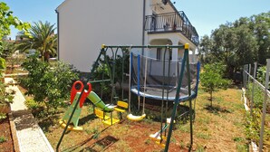 A playground with a slide and swings, a trampoline, and a building with a balcony in the background. - Apartment 1030 (Fazana)