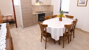 A compact kitchen with modern appliances, a dining area with a round table and wooden chairs, and a small window with a view. - Apartment 1031 (Fazana)
