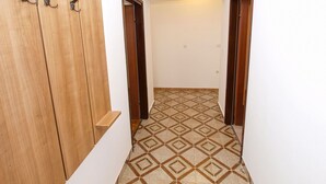 A narrow hallway with a patterned floor, wooden doors, and a wooden wardrobe with hooks. - Apartment 1031 (Fazana)